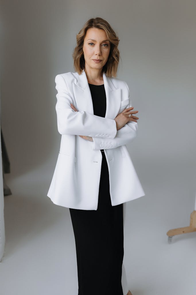 Elegant businesswoman standing confidently in a white suit with arms crossed in a professional studio setting.